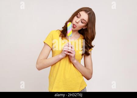 Ritratto di ragazza divertente adolescente che si stacca lingua leccarsi gelato, degustazione e gustando delizioso sapore dessert, dolce confezione. Studio interno girato isolato su sfondo grigio. Foto Stock