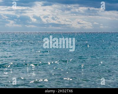 orizzonte blu del mare scintillante nei raggi del sole del mattino con nuvole morbide nel cielo Foto Stock