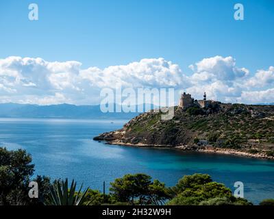 Mare e faro bianco torre vicino albero sempreverde lungo la riva fiancheggiata da montagne di Calamosca in Sardegna Italia in una giornata di sole, con cielo blu e f Foto Stock