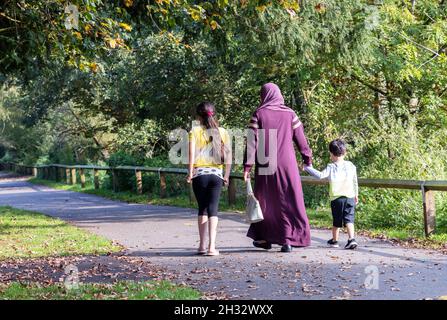 Famiglia araba Regno Unito; una madre musulmana e i suoi due bambini che camminano nel parco, visto dal retro, Salisbury Wiltshire Regno Unito Foto Stock