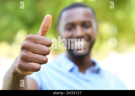 Uomo felice con la pelle nera che gesta i pollici in un parco Foto Stock