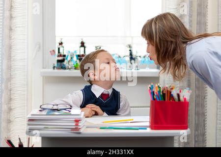 Una bella giovane madre con suo figlio sta facendo i compiti in una scrivania a casa contro uno sfondo leggero di una finestra durante una quarantena pandemica. Selez Foto Stock