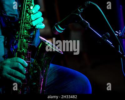 primo piano mani di artista musicista suona il sassofono in un concerto di fronte al microfono illuminato da luce verde Foto Stock