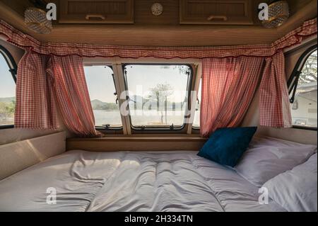 All'interno di un letto vuoto in camper e la vista attraverso la finestra con tenda sul lago al campeggio Foto Stock