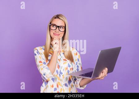 Foto di giovane donna sognante astuta indossare stampa camicia occhiali sorriso braccio mento tenendo dispositivo moderno isolato viola sfondo di colore Foto Stock