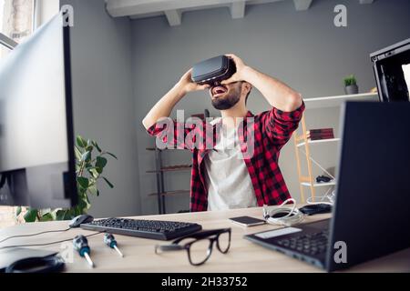 Ritratto di attraente ragazzo allegro stupito indossando cuffie per giocare video gioco a piedi simulazione al posto di lavoro stazione al chiuso Foto Stock