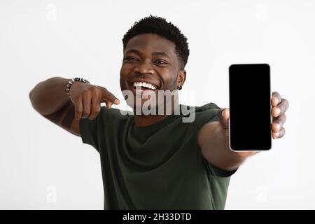 Cellulare con schermo vuoto in giovane mano uomo nero, allegro ragazzo americano africano di stile che punta al nuovo cellulare, sorridente, godendo piacevole Foto Stock