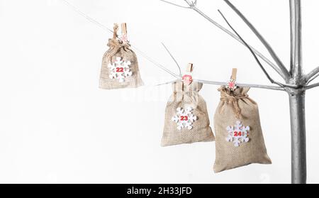 Borse fatte di matting per regali con i numeri 22, 23 e 24 su di loro appesi su clothespins su albero alternativo di Natale fatto di legno dipinto d'argento su bianco Foto Stock