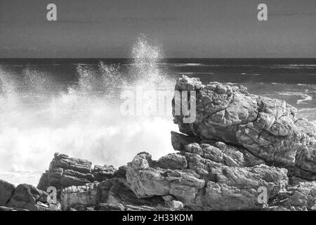 Spruzzi dalle onde forti in bianco e nero lungo la costa rocciosa della sezione di Tsitsikamma nel Parco Nazionale del percorso del giardino del Sudafrica Foto Stock