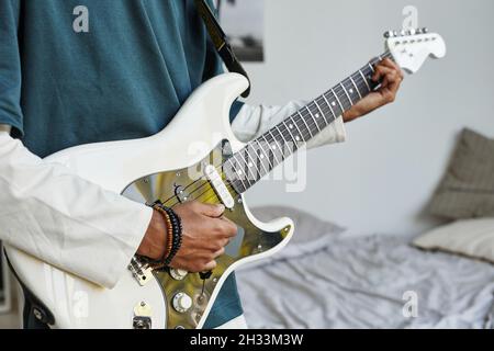 Primo piano di un adolescente afro-americano che suona la chitarra elettrica a casa, copy space Foto Stock