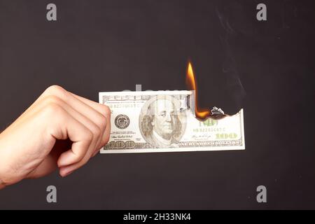 La mano tiene il dollaro che brucia isolato su uno sfondo nero. Foto Stock