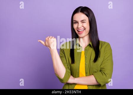 Foto di bella ragazza flirty vestita vestiti verdi che girano il pollice puntando su spazio vuoto sorridendo isolato viola sfondo di colore Foto Stock