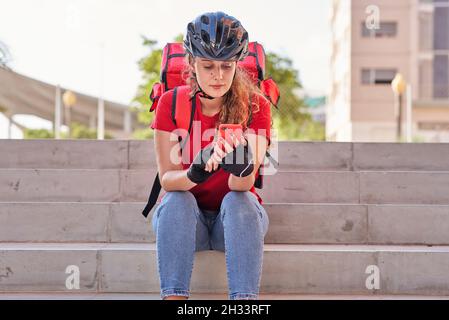 Una ragazza di consegna seduta sulle scale in attesa del prossimo ordine Foto Stock