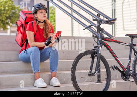 Una ragazza di consegna seduta sulle scale in attesa del prossimo ordine Foto Stock