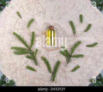 Piccola bottiglia di vetro con olio essenziale di abete rosso aromatico di conifere spa con rametti verdi intorno ad esso al centro del taglio della sega di legno. Aromaterapia di Natale un Foto Stock