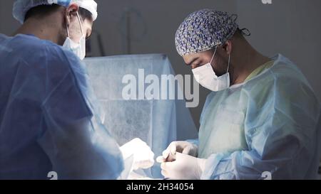 Dettagli di un vero e proprio intervento chirurgico in sala operatoria sterile. Azione. Sfondo medico di medici che indossano uniforme sterile e maschera facciale al lavoro al Foto Stock