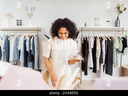 Donna elegante in boutique scelta cintura. Giovane donna in piedi in un negozio di abbigliamento locale alla ricerca di accessori. Foto Stock