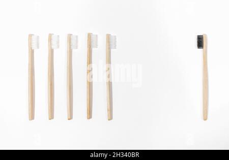 Fila di spazzolini bianchi eco-compatibili in bambù naturale contro un nero su bianco. Concetto minimo creativo di confronto individ e maggioranza. Plas Foto Stock