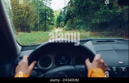 Conducente vestito giacca arancione brillante guida una moderna fuoristrada guida a sinistra guida a sinistra LHD sulla strada di campagna verde montagna foresta. POV all'interno del vento dell'automobile Foto Stock