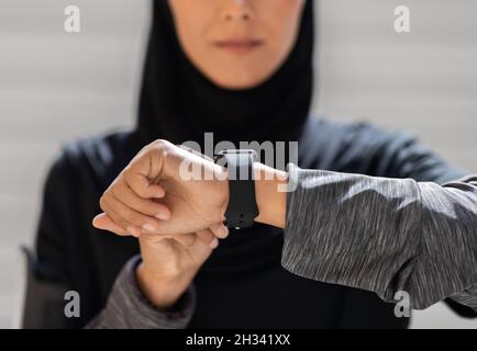Concetto di gadget sportivi. Donna musulmana irriconoscibile in Hijab controllare la sua attività di fitness su Smartwatch mentre si allena all'aperto, Madonna Islamica usando Mo Foto Stock