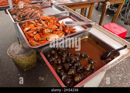 Vassoi di lumache cotte, artigli di granchio e gamberi in vendita in una cucina all'aperto sulla strada di Shanghai. Foto Stock