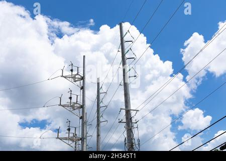 Elaborati poli di potenza in metallo con pile di linee elettriche contro un cielo blu brillante con nuvole bianche brillanti, aspetto orizzontale Foto Stock