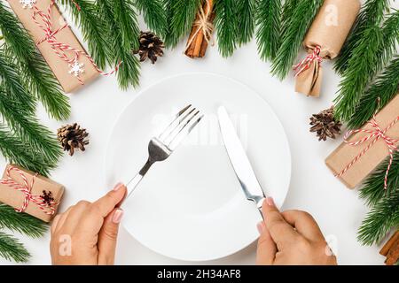 Set da tavolo per feste di Natale. Le mani femminili tengono un coltello d'argento e una forcella sopra la piastra vuota bianca Foto Stock