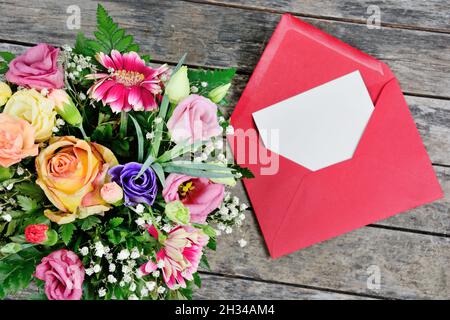 La carta bianca bianca bianca bianca è posta sulla busta di carta rossa aperta ed il bouquet del fiore su un tavolo del legno Foto Stock