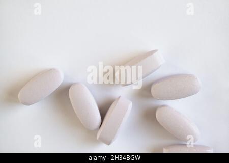 Vitamine lunghe o pillole bianche o grigie su sfondo bianco, macro, primo piano, spazio copia, piano. Integratori nutrizionali concetto, salute, vitamine Foto Stock