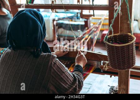 Donna tessendo un tessuto con su telaio pedale tradizionale. Artigianato artigianale Foto Stock