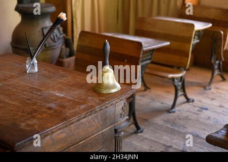 Un campanello siede sulla scrivania dell'insegnante in una sala ricreata del XIX secolo al museo di storia vivente El Rancho de las Golondrinas nel New Mexico USA. Foto Stock