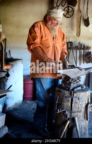 Un fabbro lavora con un ferro e un incudine nel negozio di fabbri al museo di storia vivente El Rancho de las Golondrinas vicino a Santa Fe, New Mexico. Foto Stock