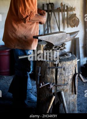 Un fabbro lavora con un ferro e un incudine nel negozio di fabbri al museo di storia vivente El Rancho de las Golondrinas vicino a Santa Fe, New Mexico. Foto Stock