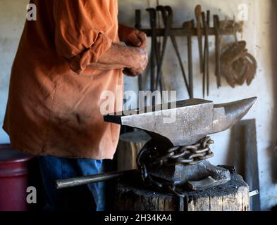 Un fabbro lavora con un ferro e un incudine nel negozio di fabbri al museo di storia vivente El Rancho de las Golondrinas vicino a Santa Fe, New Mexico. Foto Stock