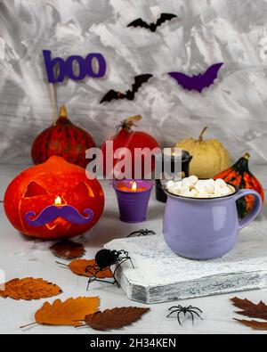 Vita concettuale morta sul tema di Halloween. Tazza lilla con caffè e marshmallows su sfondo di zucca con baffi lilla di Halloween su un Foto Stock