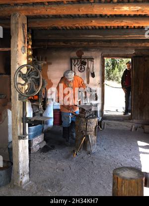 Un fabbro lavora con un ferro e un incudine nel negozio di fabbri al museo di storia vivente El Rancho de las Golondrinas vicino a Santa Fe, New Mexico. Foto Stock