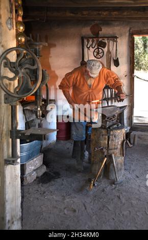 Un fabbro lavora con un ferro e un incudine nel negozio di fabbri al museo di storia vivente El Rancho de las Golondrinas vicino a Santa Fe, New Mexico. Foto Stock