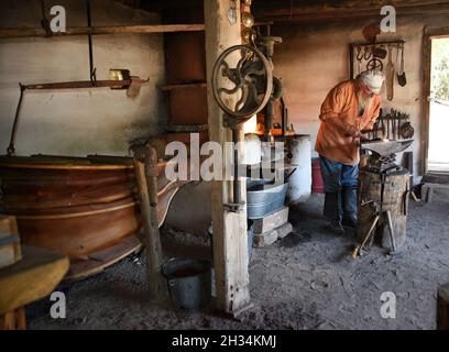 Un fabbro lavora con un ferro e un incudine nel negozio di fabbri al museo di storia vivente El Rancho de las Golondrinas vicino a Santa Fe, New Mexico. Foto Stock