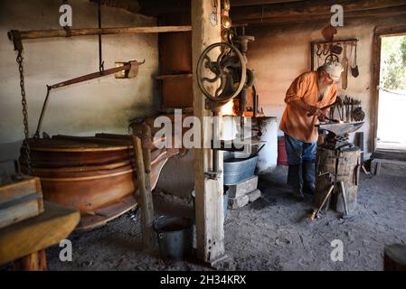 Un fabbro lavora con un ferro e un incudine nel negozio di fabbri al museo di storia vivente El Rancho de las Golondrinas vicino a Santa Fe, New Mexico. Foto Stock