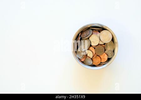 Selezione assortita di monete americane di uso corrente in una tazza di cromo su uno sfondo bianco con spazio di copia; centesimi, dime, quarti, nickel degli Stati Uniti. Foto Stock