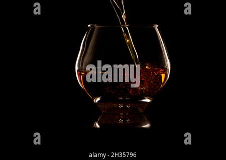 Versare il whiskey in un bicchiere di roccia su sfondo nero Foto Stock