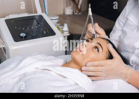 Vista laterale della donna che riceve la terapia di microdermoabrasione sulla fronte alla beauty spa. Trattamento di ringiovanimento. Viso di bellezza. Cosmetologia procedura di bellezza. Foto Stock