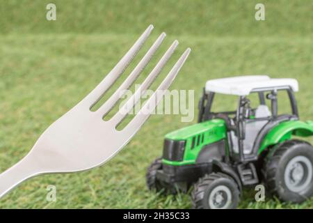 Trattore giocattolo piccolo su erba finta/finta con denti delle forche in acciaio inox. Per produzione di alimenti nel Regno Unito, da azienda agricola a forca, da campo a forca/da campo a piastra. Foto Stock