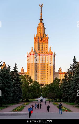Mosca, Russia - 17 settembre 2017: Edificio principale della torre iconica dell'università statale di Mosca che tocca la luce solare arancione e le persone che camminano intorno al parco Foto Stock