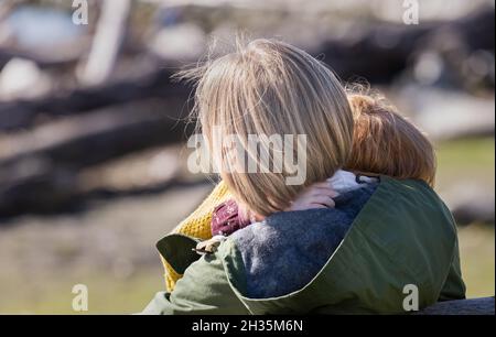 La vista posteriore di una madre abbraccia il suo piccolo bambino all'aperto nel parco. Famiglia di benessere felice o mamma nuova per il concetto adottato bambino. Vista stradale, selettiva Foto Stock