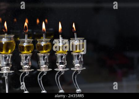 Le candele Hanukkah fatte di olio d'oliva sono illuminate in una menora d'argento sullo sfondo delle tenebre della notte Foto Stock