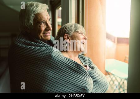 Coppia anziana in piedi a casa di fronte alla finestra e guardando fuori - concetto di romantica coppia pensionato amarsi a vicenda Foto Stock