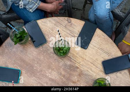 gruppo di femmine che hanno i loro smartphone giù su un tavolo mentre godendo un cocktail e l'azienda. Le donne online insieme. Vista dall'alto di amici multirazziali in cerchio utilizzando il telefono wifi in caffetteria. Foto di alta qualità Foto Stock