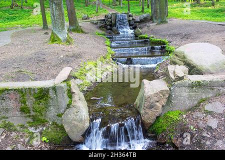 Una cascata di un ruscello scorre su gradini di pietra in un parco cittadino. Europa Foto Stock