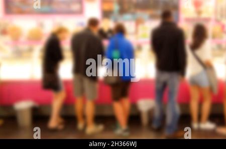 Immagine di sfondo sfocata di persone in attesa di un bancone per ordinare il cibo dalla vetrina - in una gelateria, un negozio di dolci, un negozio di dessert. Foto Stock